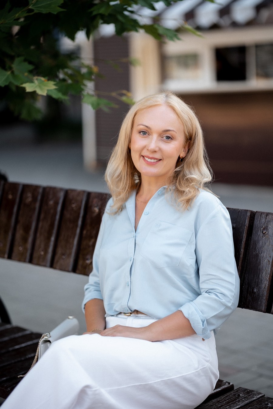 Svitlana seated outdoors in a pale blue shirt, hands resting in her lap, listening attentively