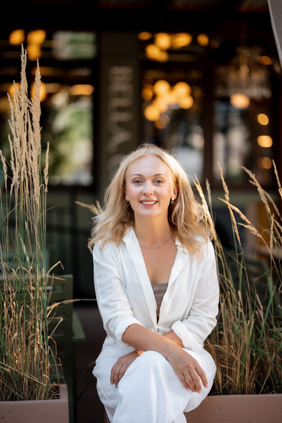 Svitlana sitting among tall grasses in the evening light, wearing white